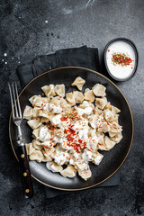 Wall Mural - Turkish manti with yoghurt and tomato sauce in a plate. Black background. Top view