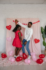 Wall Mural - Romantic young African couple dancing on pink fabric background with heart shaped balloons