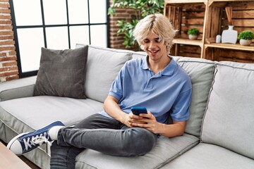 Poster - Young blond man using smartphone sitting on sofa at home