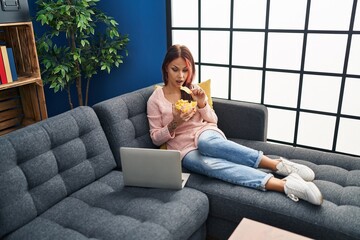 Wall Mural - Young caucasian woman watching movie eating chips potatoes at home