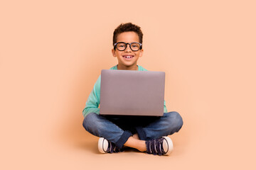 Poster - Full size photo of positive smart little boy sit floor use wireless laptop isolated on beige color background