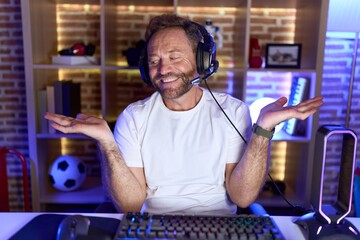 Sticker - Middle age man with beard playing video games wearing headphones smiling showing both hands open palms, presenting and advertising comparison and balance