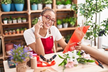 Canvas Print - Young beautiful hispanic woman florist talking on smartphone reading clipboard at florist