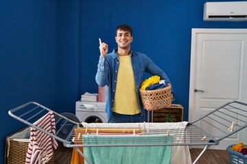 Wall Mural - Young hispanic man hanging clothes at clothesline smiling happy pointing with hand and finger to the side