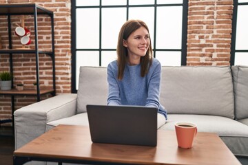 Sticker - Young blonde woman using laptop sitting on sofa at home