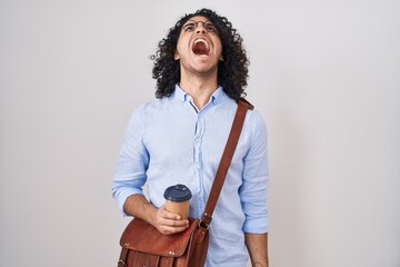 Wall Mural - Hispanic man with curly hair drinking a cup of take away coffee angry and mad screaming frustrated and furious, shouting with anger. rage and aggressive concept.