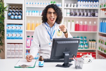 Poster - Hispanic man with curly hair working at pharmacy drugstore pointing displeased and frustrated to the camera, angry and furious with you