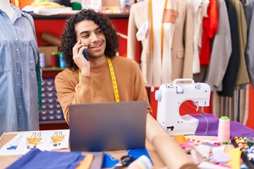 Poster - Young latin man tailor talking on smartphone using laptop at atelier