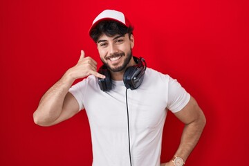 Poster - Hispanic man with beard wearing gamer hat and headphones smiling doing phone gesture with hand and fingers like talking on the telephone. communicating concepts.