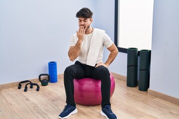 Poster - Hispanic man with beard sitting on pilate balls at yoga room bored yawning tired covering mouth with hand. restless and sleepiness.