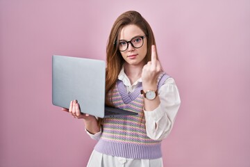 Wall Mural - Young caucasian woman working using computer laptop showing middle finger, impolite and rude fuck off expression