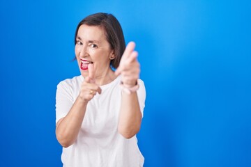 Canvas Print - Middle age hispanic woman standing over blue background pointing fingers to camera with happy and funny face. good energy and vibes.