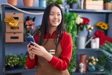 Canvas Print - Young chinese woman florist smiling confident using smartphone at flower shop