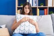 © Krakenimages.com - Hispanic woman hugging pillow sitting on the sofa skeptic and nervous, frowning upset because of problem. negative person.