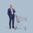© stokkete - Pensive businessman standing behind a shopping cart