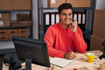 Canvas Print - Young hispanic man ecommerce business worker talking on smartphone writing on notebook at office