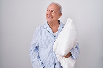 Canvas Print - Senior man with grey hair wearing pijama hugging pillow smiling looking to the side and staring away thinking.