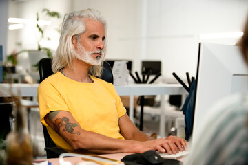 Wall Mural - Adult long gray hair man using computer while sitting at office desk