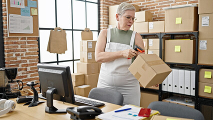 Poster - Middle age grey-haired woman ecommerce business worker scanning package using computer at office