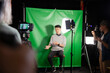 © PhotoAlto - Young adult man giving an interview while sitting against green screen