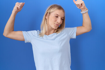 Poster - Young caucasian woman wearing casual blue t shirt showing arms muscles smiling proud. fitness concept.