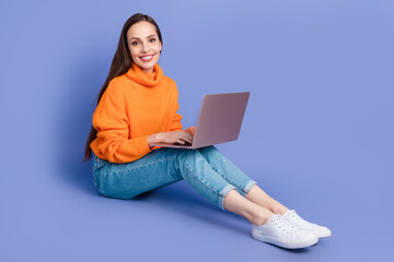 Poster - Full size body photo of cheerful young lady wear knitted orange pullover work in coworking with laptop isolated on purple color background