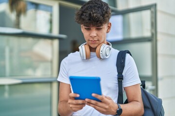 Poster - Young hispanic teenager student using touchpad with relaxed expression at university