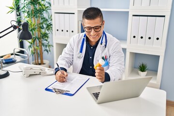 Poster - Young latin man doctor writing on document holding pills at clinic