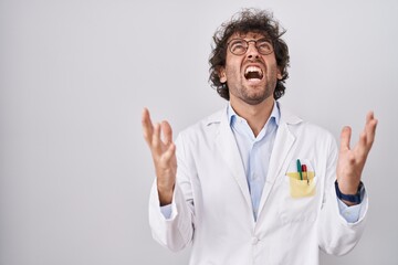 Wall Mural - Hispanic young man wearing doctor uniform crazy and mad shouting and yelling with aggressive expression and arms raised. frustration concept.