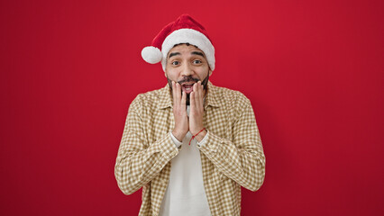 Sticker - Young hispanic man surprise expression wearing christmas hat over isolated red background