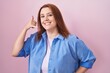 © Krakenimages.com - Young hispanic woman with red hair standing over pink background smiling doing phone gesture with hand and fingers like talking on the telephone. communicating concepts.