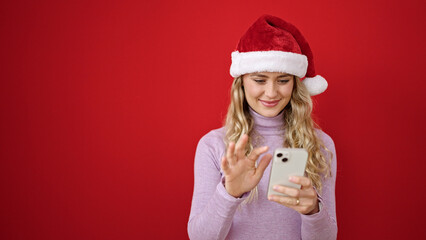 Sticker - Young blonde woman wearing christmas hat using smartphone over isolated red background