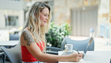 Poster - Young blonde woman using laptop taking notes smiling at coffee shop terrace