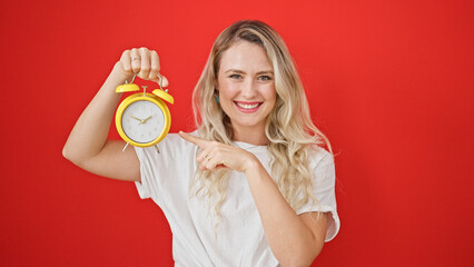 Sticker - Young blonde woman smiling confident pointing to alarm clock over isolated red background