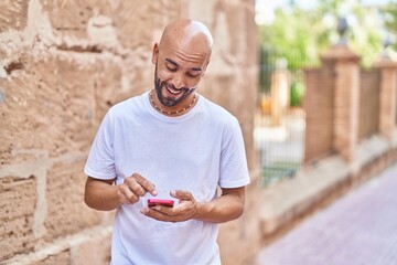 Wall Mural - Young bald man smiling confident using smartphone at street