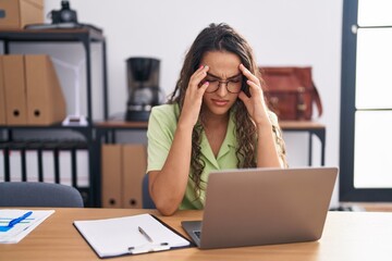 Poster - Young hispanic woman working at the office wearing glasses with hand on head for pain in head because stress. suffering migraine.