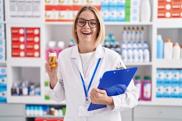 Canvas Print - Young caucasian woman working at pharmacy drugstore holding pills smiling and laughing hard out loud because funny crazy joke.