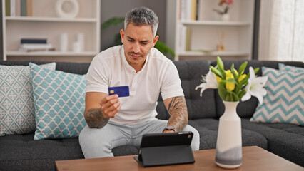 Wall Mural - Young hispanic man shopping with touchpad and credit card at home