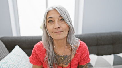 Poster - Captivating indoor shot of a beautiful, grey-haired middle age woman, deeply engrossed in relaxation, sitting comfortably in her cozy living room on a snug sofa with a serious, concentrated expression