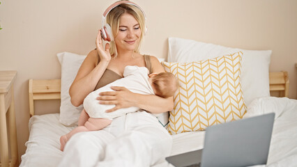 Poster - Mother and daughter sitting on bed breastfeeding baby listening to music at bedroom