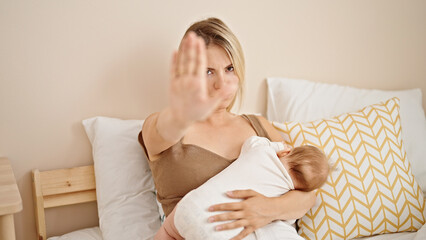 Poster - Mother and daughter sitting on bed breastfeeding baby doing stop gesture at bedroom