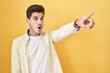 © Krakenimages.com - Young hispanic man standing over yellow background pointing with finger surprised ahead, open mouth amazed expression, something on the front