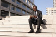 African businessman sitting on steps with digital tablet, outdoor near office building