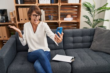 Sticker - Brunette woman doing online session at consultation office celebrating victory with happy smile and winner expression with raised hands