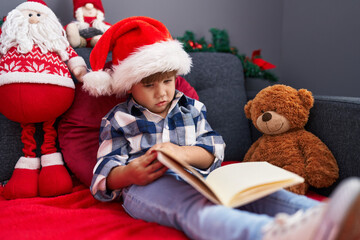  Adorable hispanic boy reading book sitting on sofa by christmas decoration at home