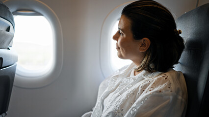 Canvas Print - Beautiful young hispanic woman smiling confident looking throw the window on the plane