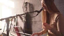 Beautiful Musician Woman Sings And Plays Synthesizer At Rehearsal For Performance With Her Music Band In Recording Studio. Voice Training And Teaching By Professional Artist Singer.