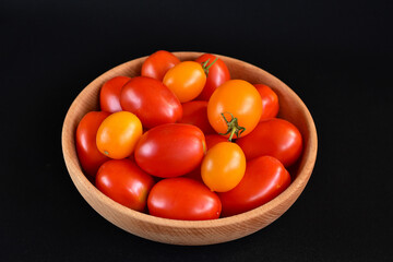 Wall Mural - yellow and red tomatoes in a wooden bowl, black background, close-up, no people