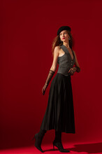 Fashionable Confident Woman Wearing Beret, Mesh Gloves, Waistcoat, Pleated Midi Skirt, High Heel Sock Boots, Posing On Red Background. Full-length Studio Fashion Portrait. Copy, Empty Space For Text