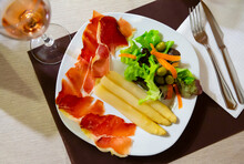 Slices Of Jamon Served With Asparagus, Lettuce And Carrot On White Plate In Restaurant.